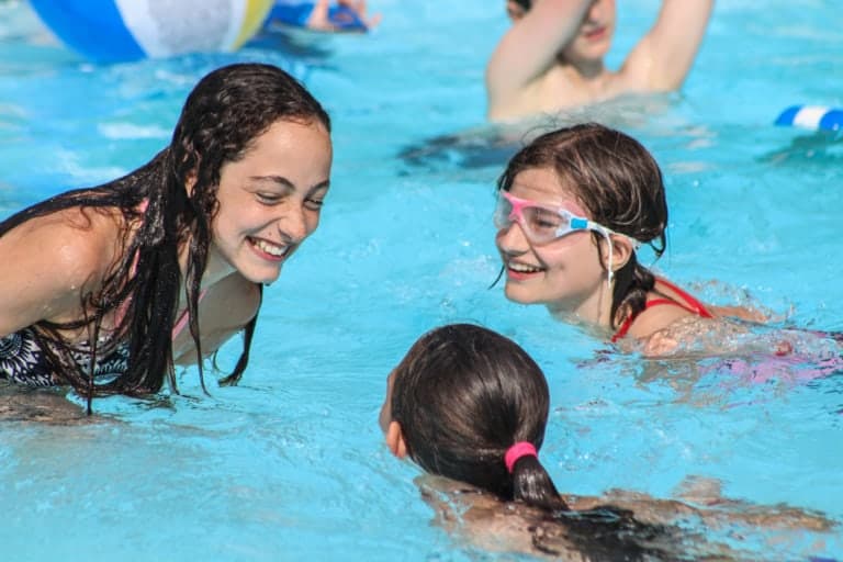 Eden Village Camp kids enjoying a fun swimming activity at the outdoor pool in a summer camp setting.