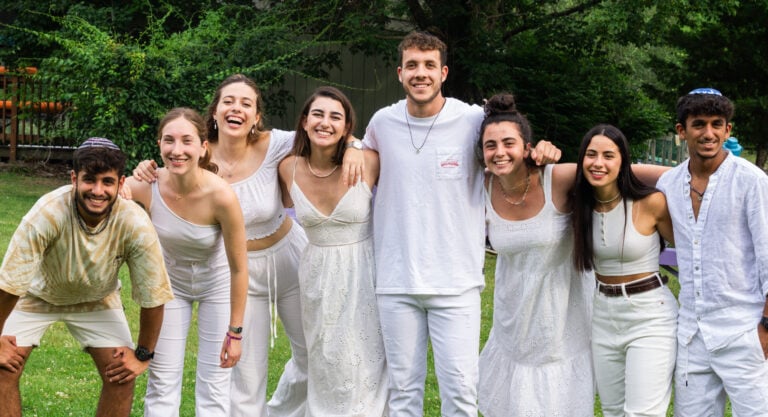 Group of eight young adults in white attire smiling outdoors.