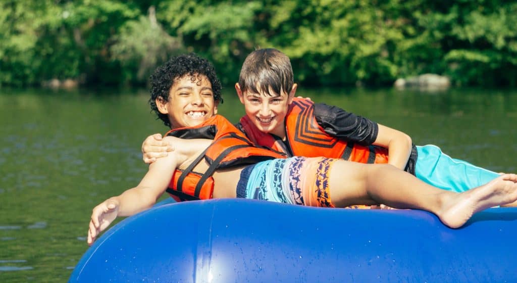 Two children joyfully lounging on a blue inflatable in a lake.