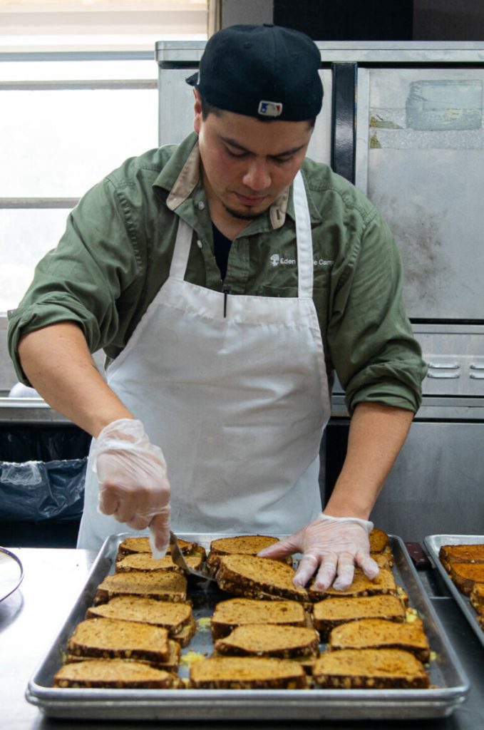 Person in an apron preparing slices of bread in a kitchen.