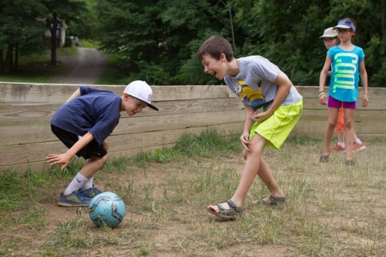 Kids playing soccer at Eden Village Camp, outdoor youth camp with nature activities, fostering friendship and teamwork in a fun, eco-friendly environment in the woods.