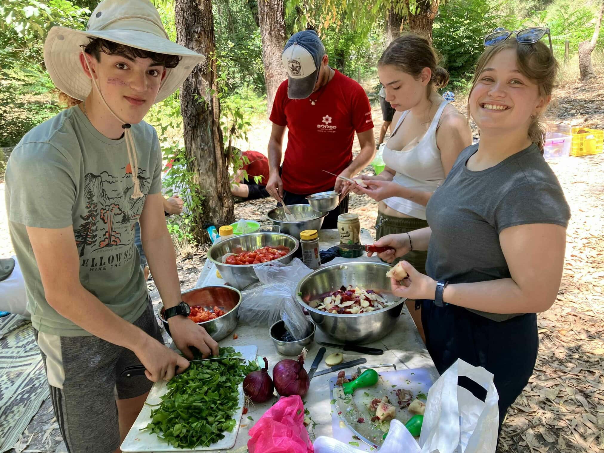 Group preparing food outdoors, surrounded by trees and bowls.