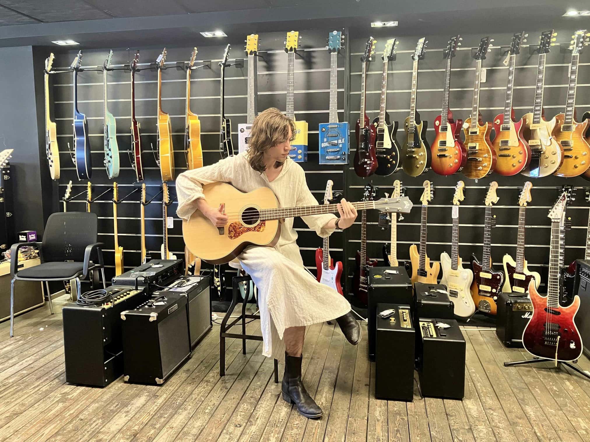 A person playing an acoustic guitar in a music store filled with various guitars.