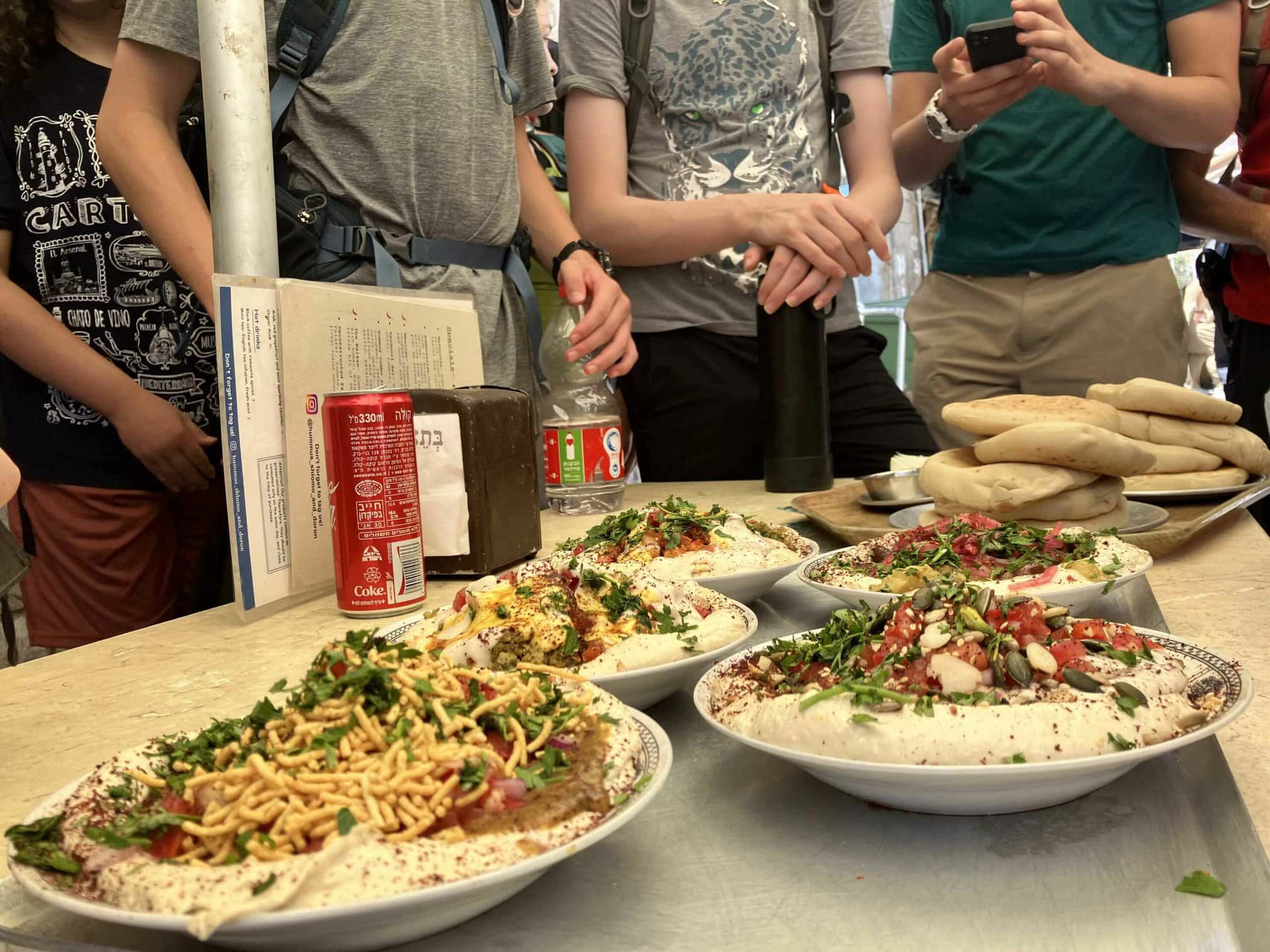 A table with various colorful dishes and bread, surrounded by people.