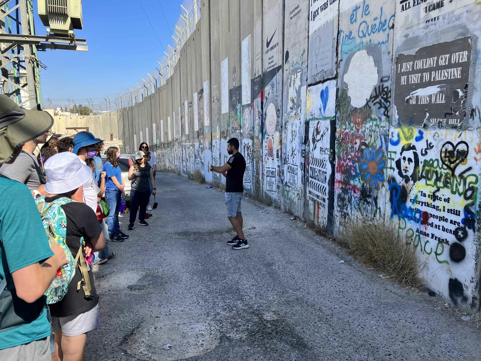 Group of individuals listening to a speaker near a graffiti-covered wall.