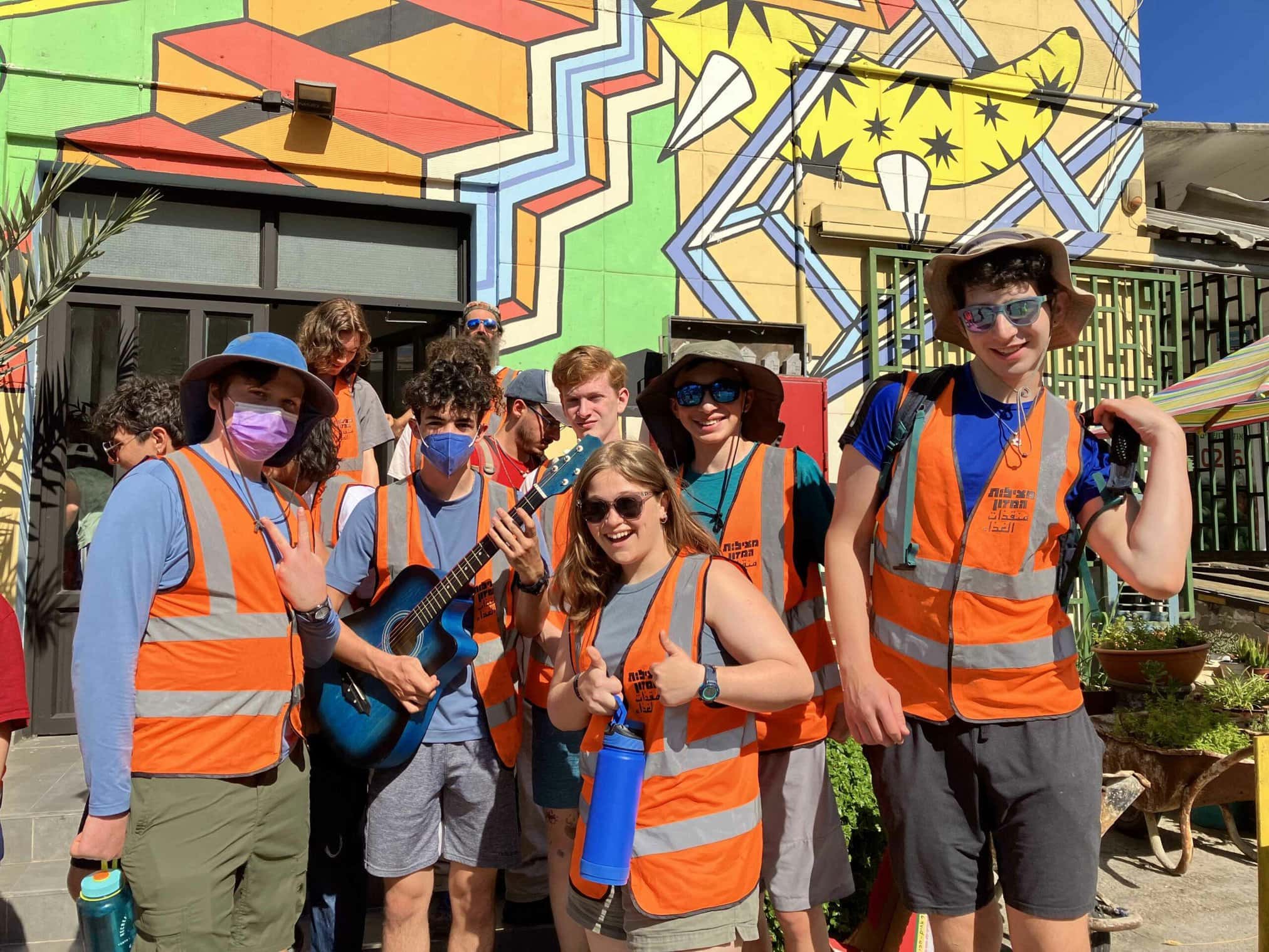 A group of individuals in bright vests smiling near a colorful mural.