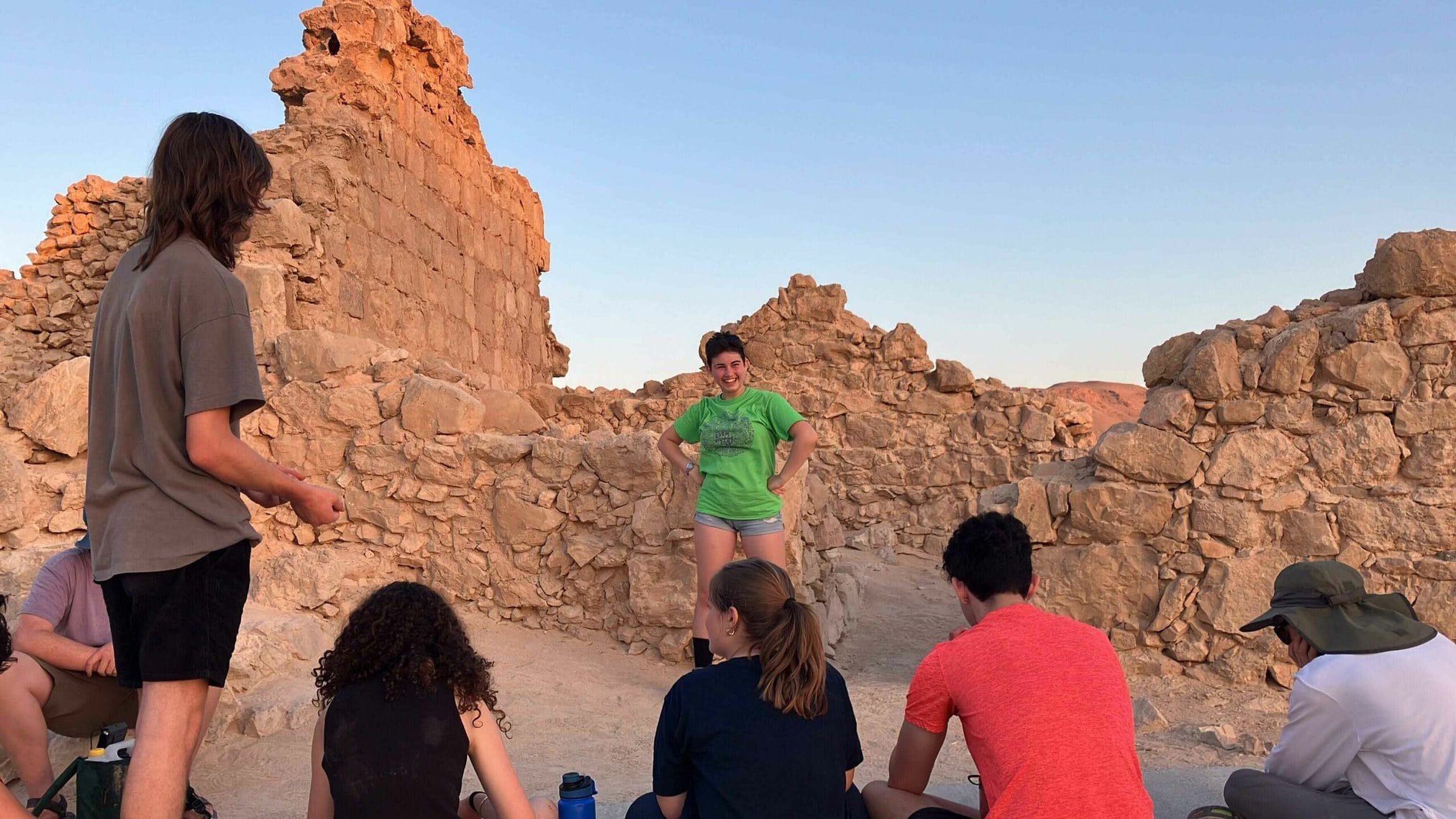 A group engaging in discussion near ancient stone ruins at sunset.