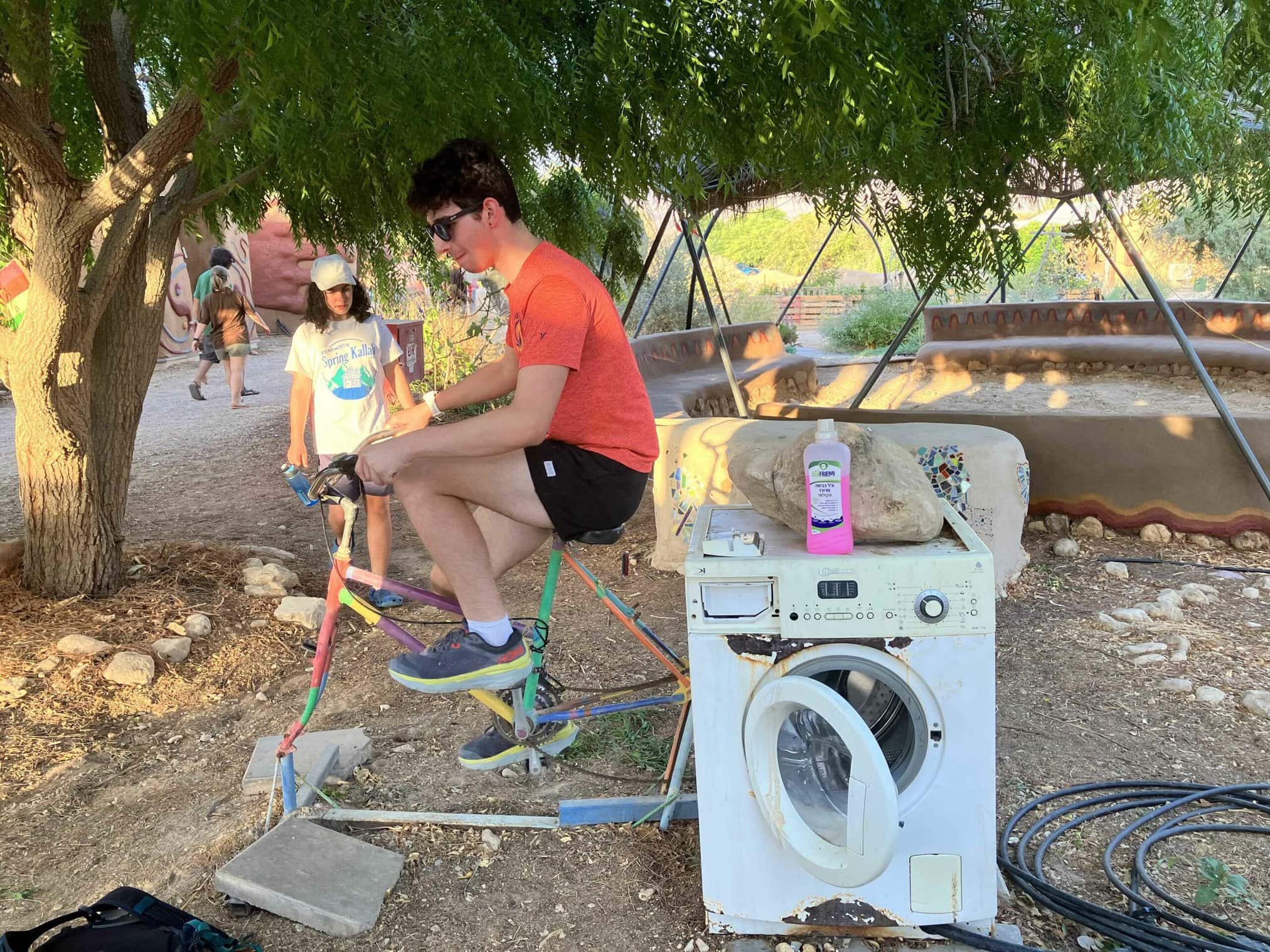 A person sitting on a colorful bike next to a washing machine outdoors.