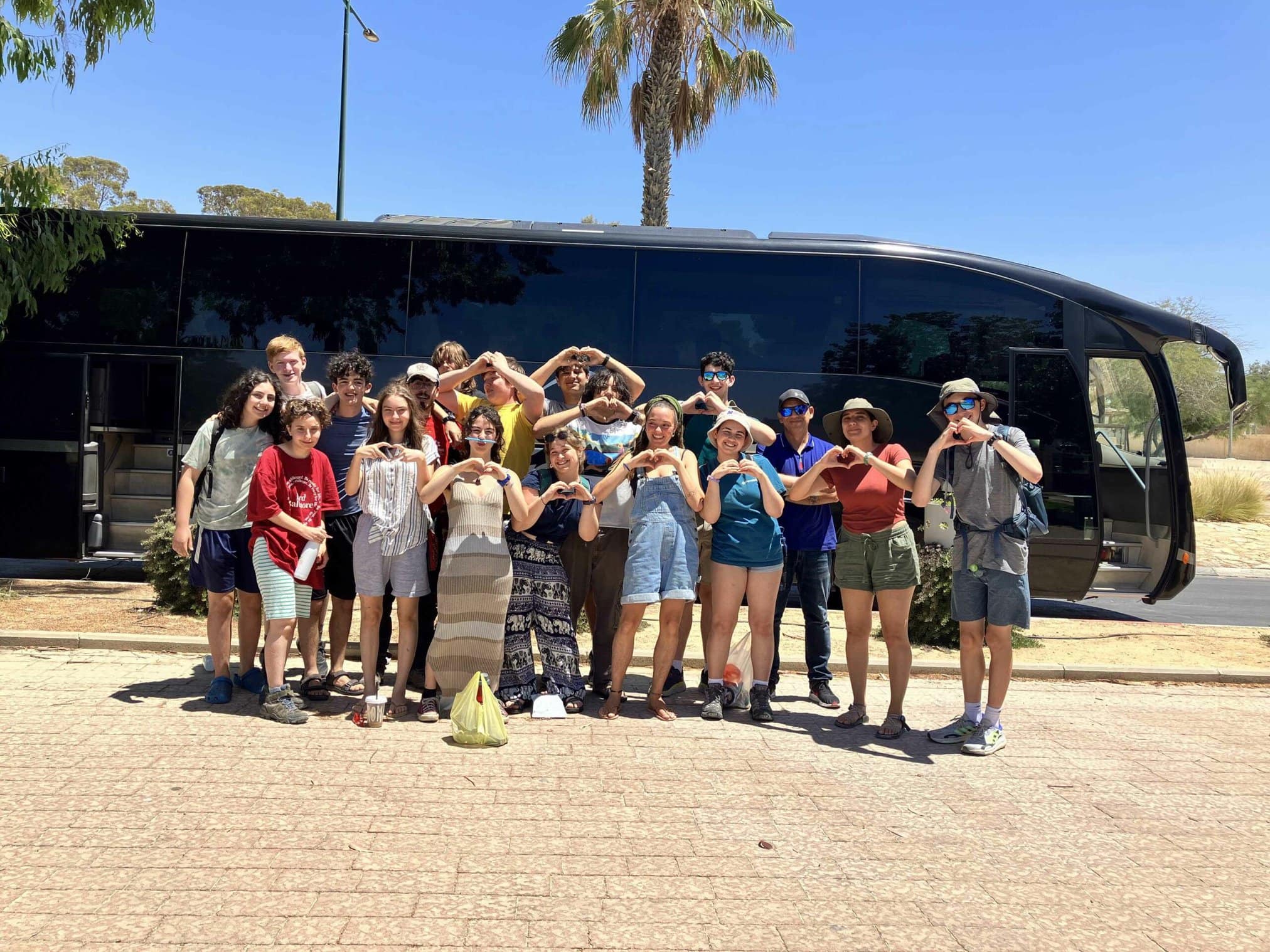 A group of diverse individuals posing playfully near a bus on a sunny day.