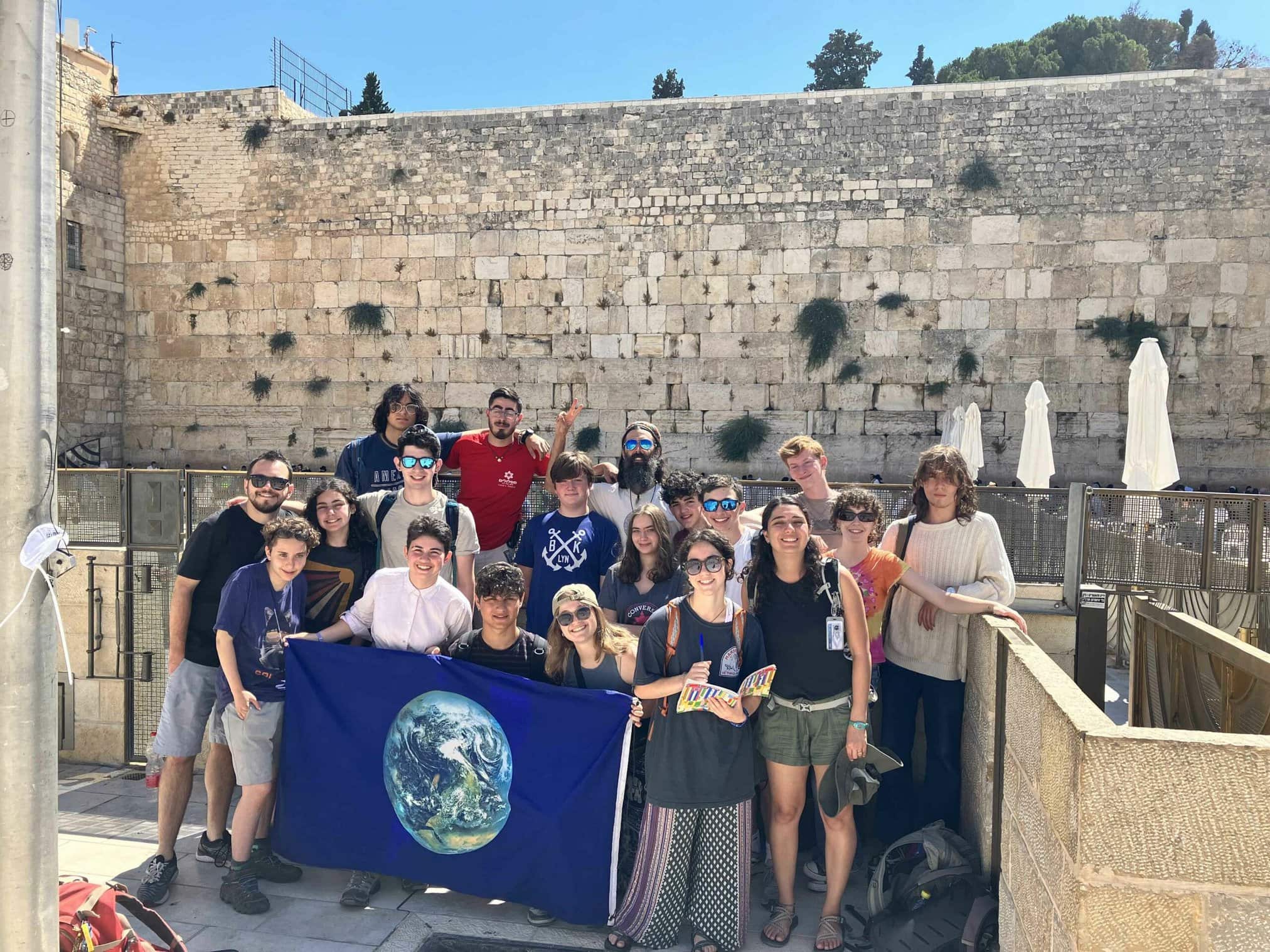 Group of diverse individuals holding an Earth flag near a stone wall.