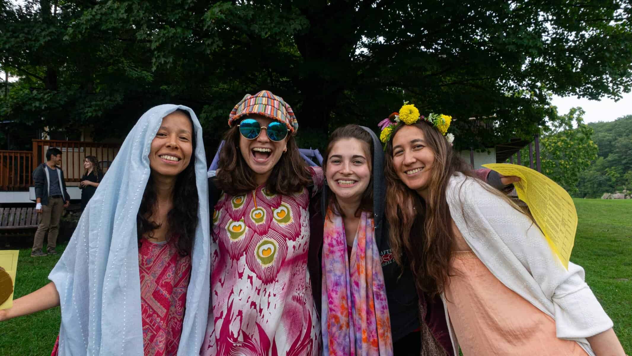 Celebrating community and creativity at Eden Village Camp, featuring diverse young women in colorful costumes and joyful expressions outdoors, promoting eco-friendly, inclusive summer camp experiences.