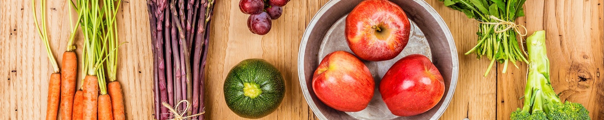 A variety of fresh vegetables and fruits on a wooden surface.