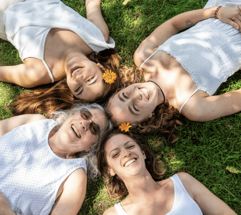 Four individuals lying on grass, smiling and enjoying the outdoors together.