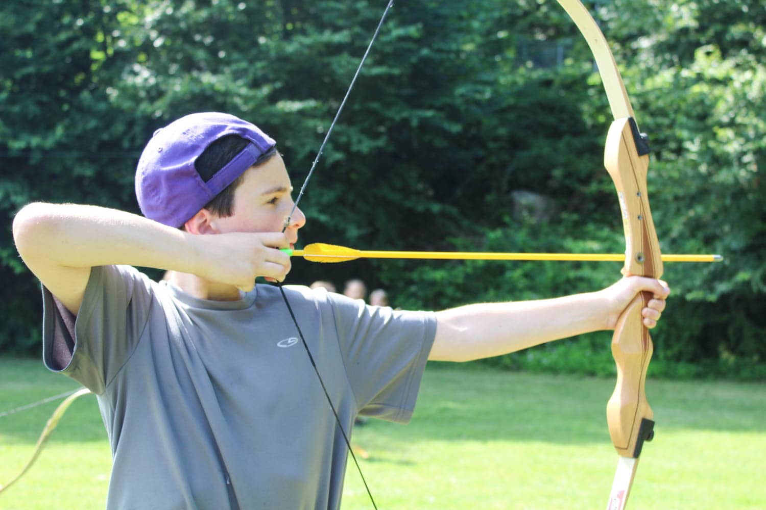 A young person aiming a bow and arrow in a green field.