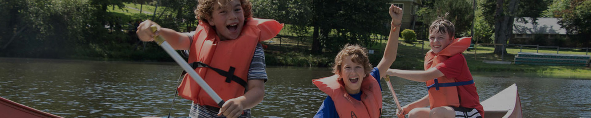 Three children in life jackets joyfully kayaking on a lake.