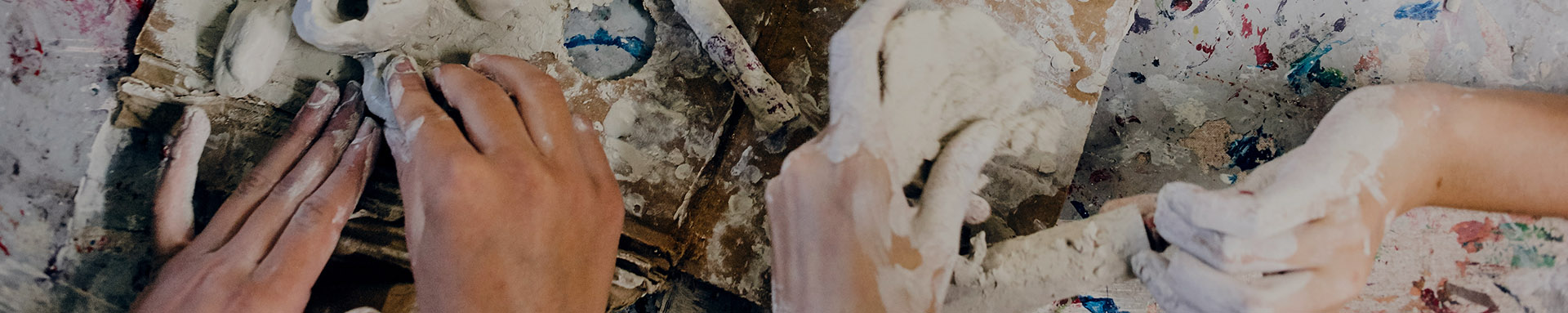 Hands shaping clay on a textured work surface with colorful splatters.